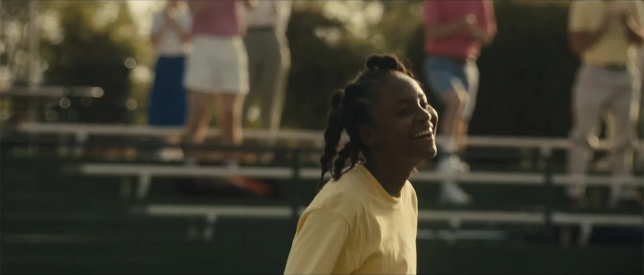 King Richard (2021) movie still: medium — A youth sports setting with metal bleachers partially visible in the blurred background. A young girl in a…