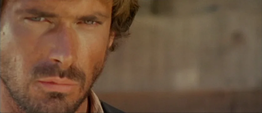 Django Kill (1967) movie still: closeup — A man stands in an outdoor area with a blurred earth-toned background. He looks ahead at the camera with a…