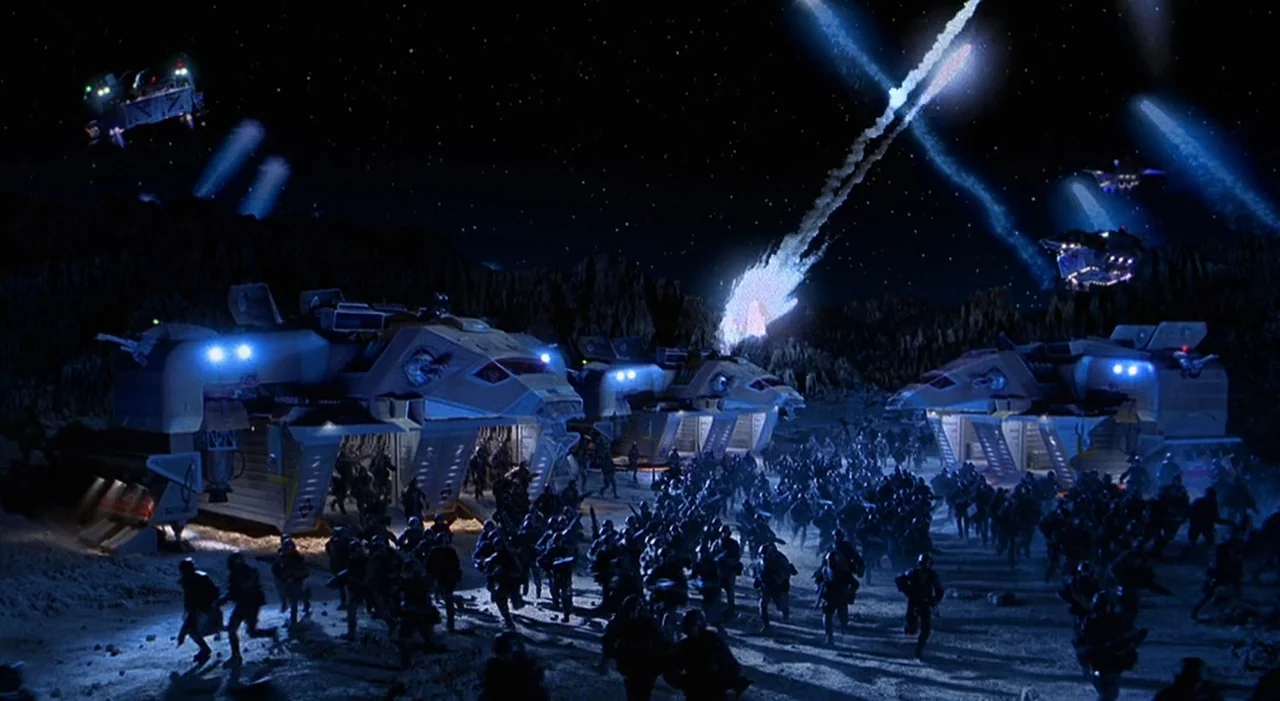 Starship Troopers (1997) movie still: wide — A dark, craggy planetary landscape at night with multiple large transport spacecraft landing on rocks.…