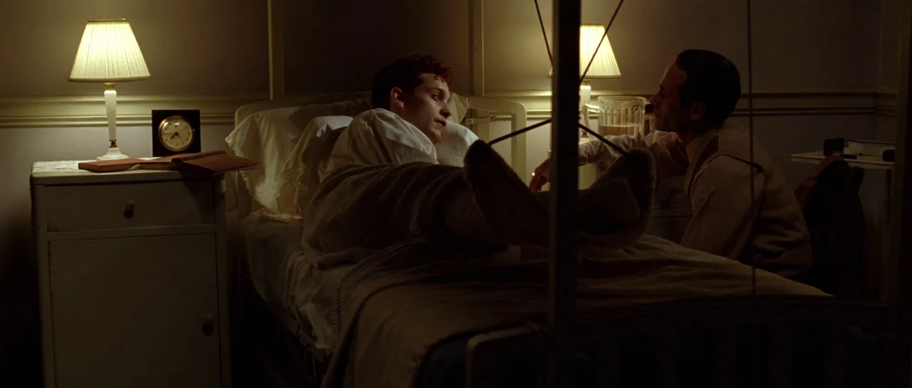 Seabiscuit (2003) movie still: medium — A dimly lit hospital room contains a patient bed and small side tables. One man sits on a chair near the bed…
