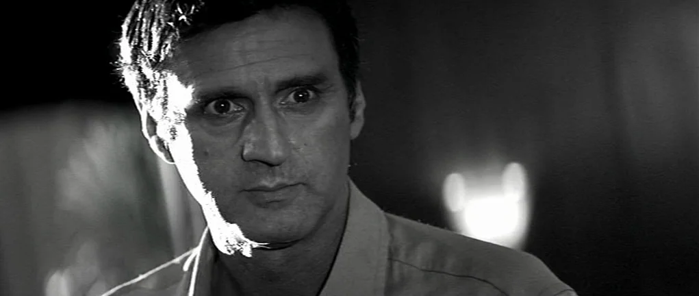 Girl on the Bridge (1999) movie still: closeup — A man stands in a dark environment with strong illumination from the side. He stares forward with…