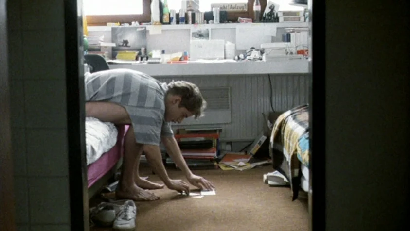 71 Fragments of a Chronology of Chance (1994) movie still: medium — A cluttered room features a desk covered in various items and books. A young man…