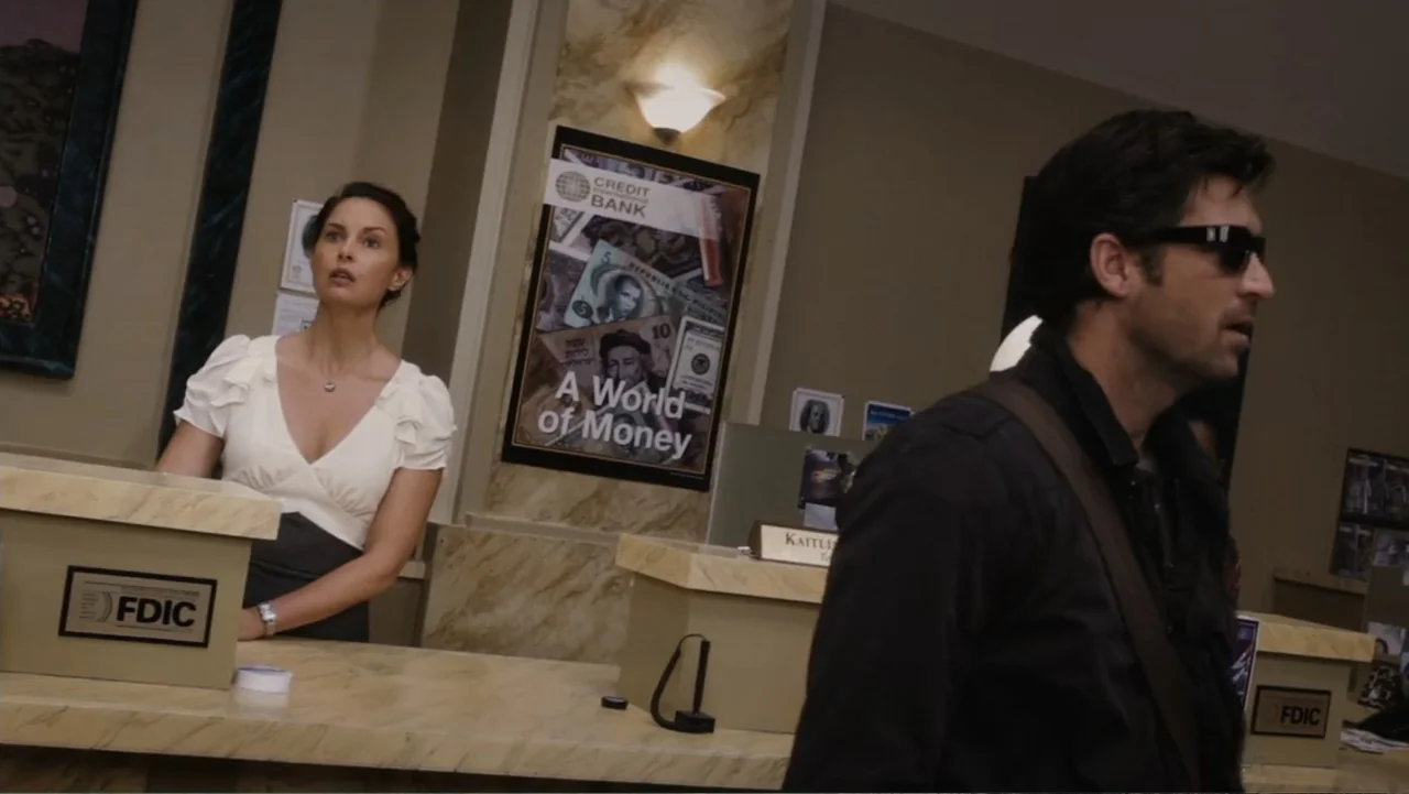 Flypaper (1999) movie still: medium — A modern bank interior features marble-look counters and promotional banking signage on the wall. A man in…