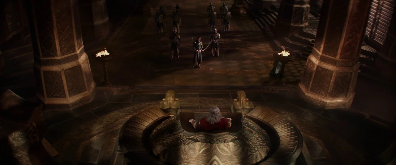Thor: The Dark World (2013) movie still: wide — A dark stone hall features massive carved columns and a central ornate elevated throne. A lone male…