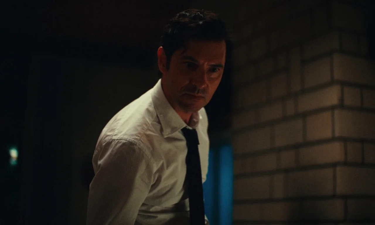 Just The Two Of Us (2023) movie still: medium — A dimly lit indoor space features a tiled wall visible on the right side. A man wearing a dress…