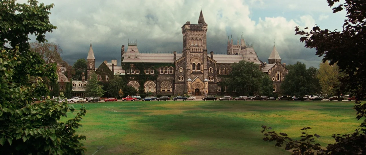 The Incredible Hulk (2008) movie still: establishing — A stone gothic revival university building faces a wide green lawn under cloudy skies.…