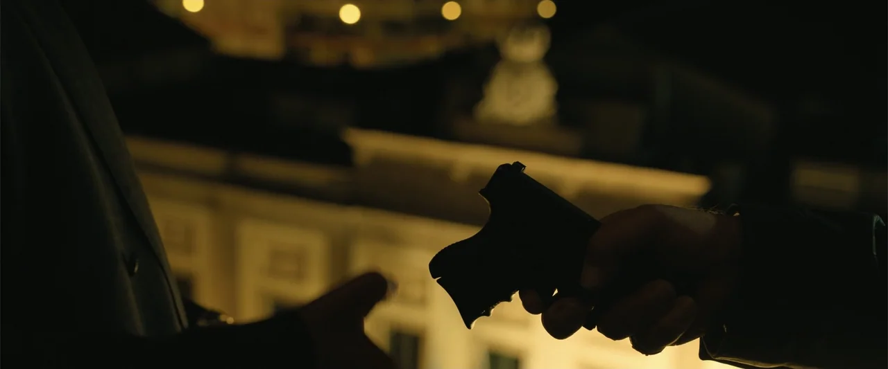 Den of Thieves 2: Pantera (2025) movie still: closeup — A dark outdoor balcony overlooks a blurred city street with illuminated building facades. A…