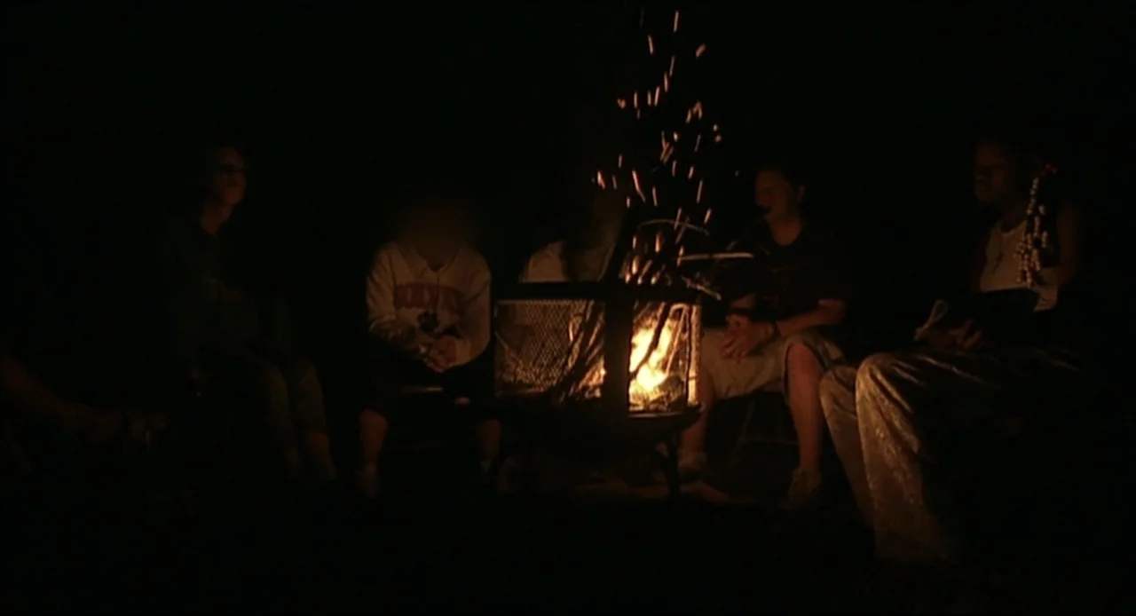 Hard as Nails (2001) movie still: medium — A group of teenagers sits in a circle outdoors at night around a fire. The flickering orange fire…