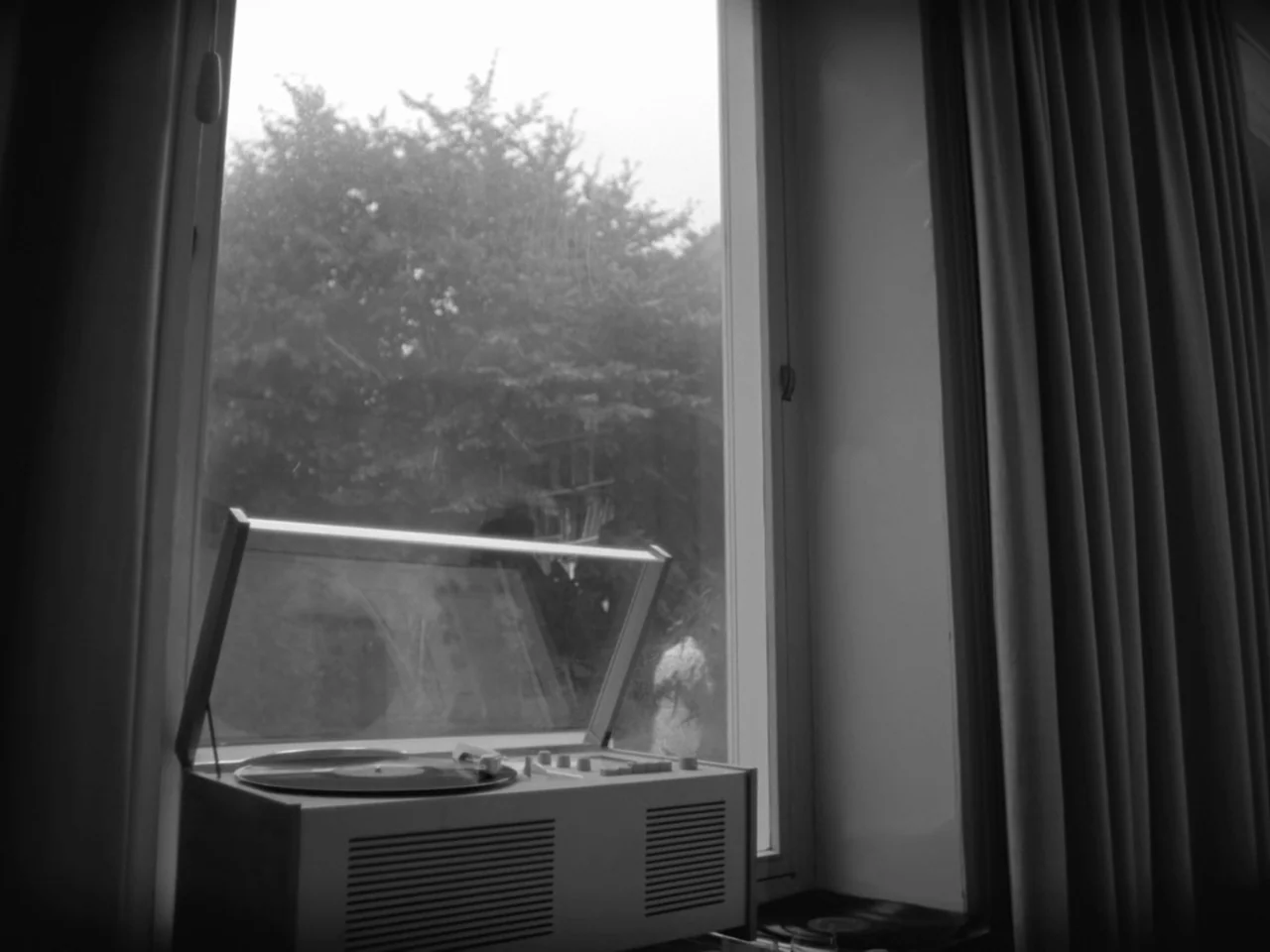 The Baby Carriage (1963) movie still: medium — A vintage record player sits on a window sill overlooking a blurry tree. Light filters through the…