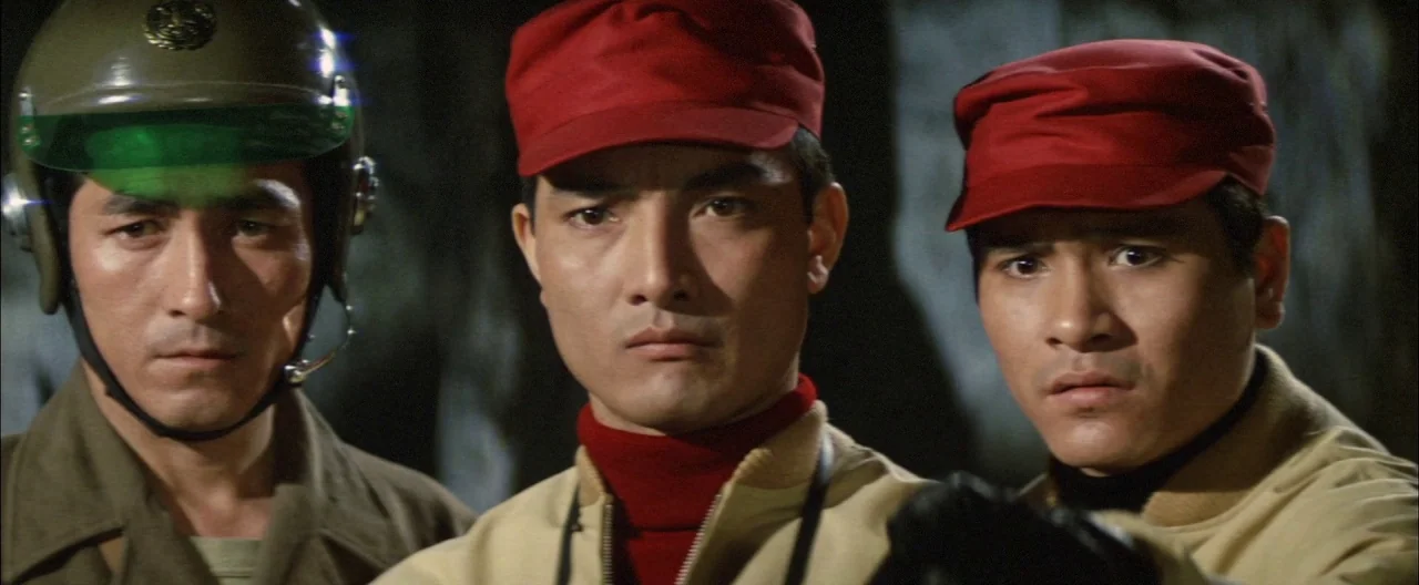 Destroy All Monsters (1968) movie still: medium — Three men stand in a dark, rocky interior space. They wear matching red caps and tan jackets while…