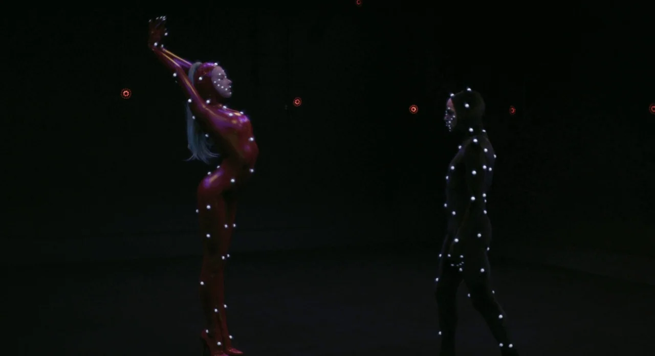 Holy Motors (2012) movie still: fullbody — A dark, empty motion capture studio with distant red LEDs embedded in the walls. Two individuals in…