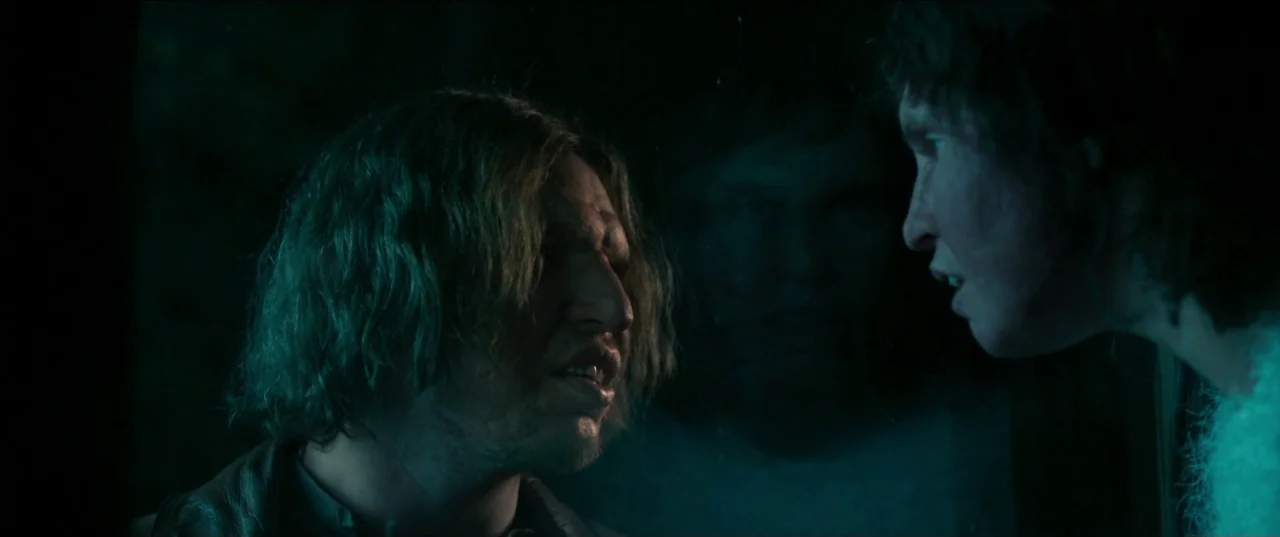 Border movie still: medium — Two men face each other from opposite sides of a dark, glass-partitioned vehicle interior. The scene is illuminated by…