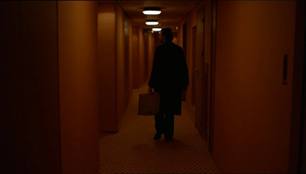 The American Friend (1977) movie still: fullbody — A long, dimly lit indoor passage features patterned carpeting and rows of recessed ceiling…