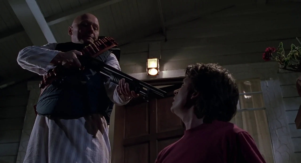 Back to the Future II (1989) movie still: medium — The front porch of a house at night with dark wood paneling and siding. A bald man stands over a…
