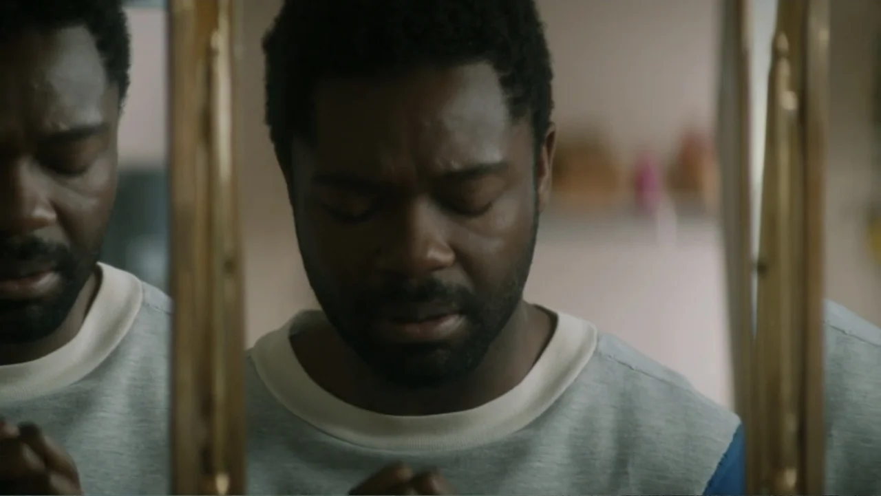 Nightingale (2014) movie still: closeup — A man stands in front of a mirror within a brightly lit indoor space. He keeps his eyes closed while his…