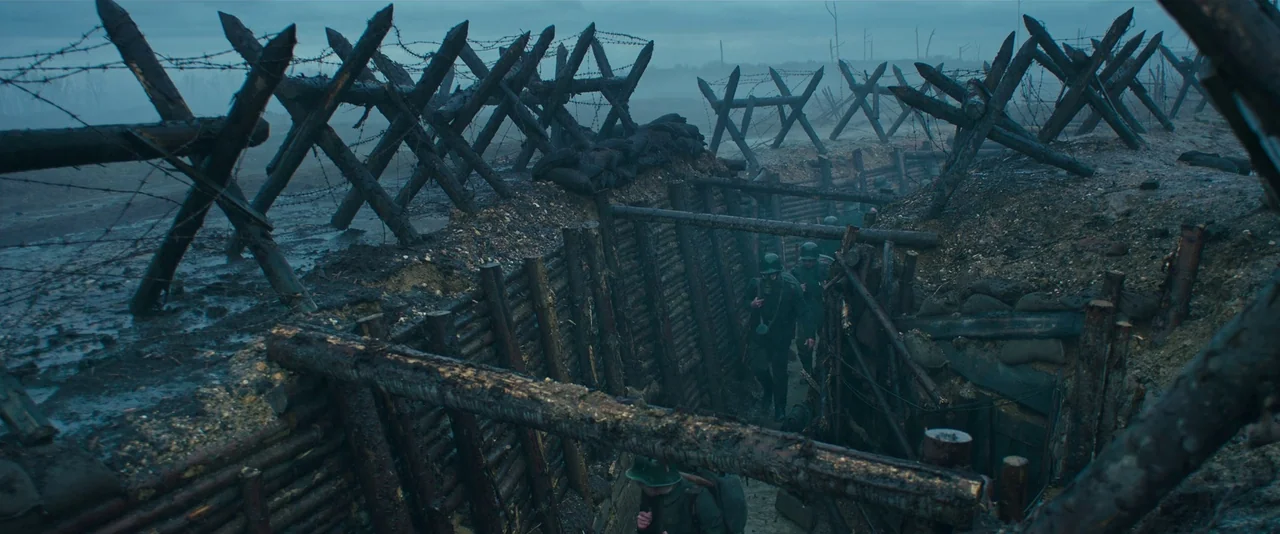 All Quiet on the Western Front (2022) movie still: wide — A muddy World War I or II battlefield trench protected by wooden stakes and wire. Several…