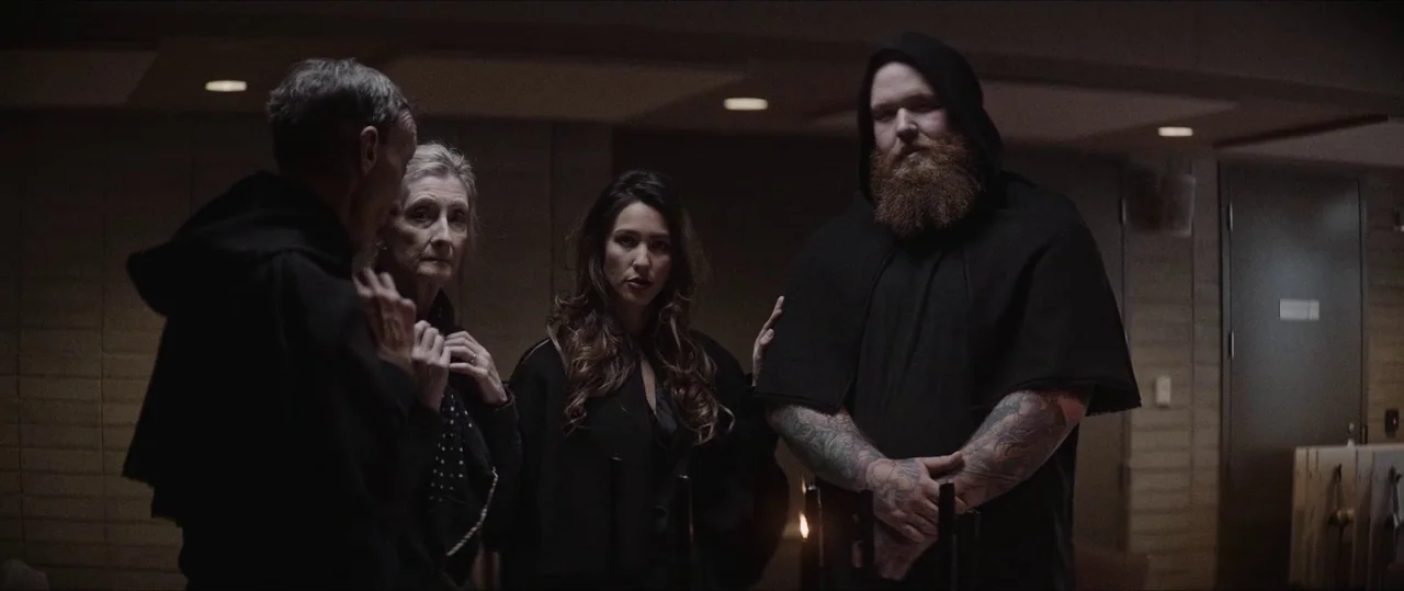 Anything For Jackson (2020) movie still: medium — A group of people wearing dark hooded robes stands in a dimly lit room. The figures gather…