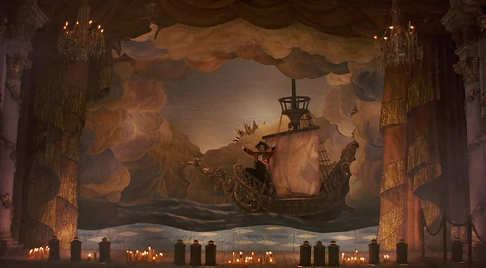 The Adventures Of Baron Munchausen (1988) movie still: wide — An ornate theatrical stage features a large painted backdrop of a ship at sea. A…