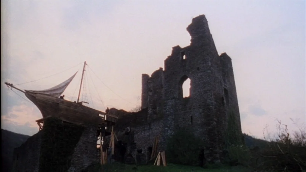 Shadow of the Vampire (2000) movie still: wide — A stone ruin stands against a pale sky at dusk. A wooden ship structure is attached to the side of…