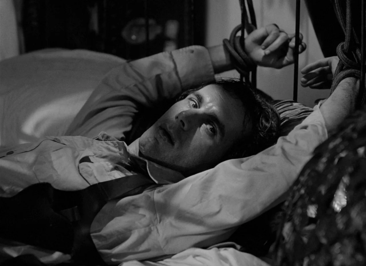 Singapore Sling (1990) movie still: closeup — A man lies on a mattress with his wrists secured to metal bars. He gazes upward with eyes wide.