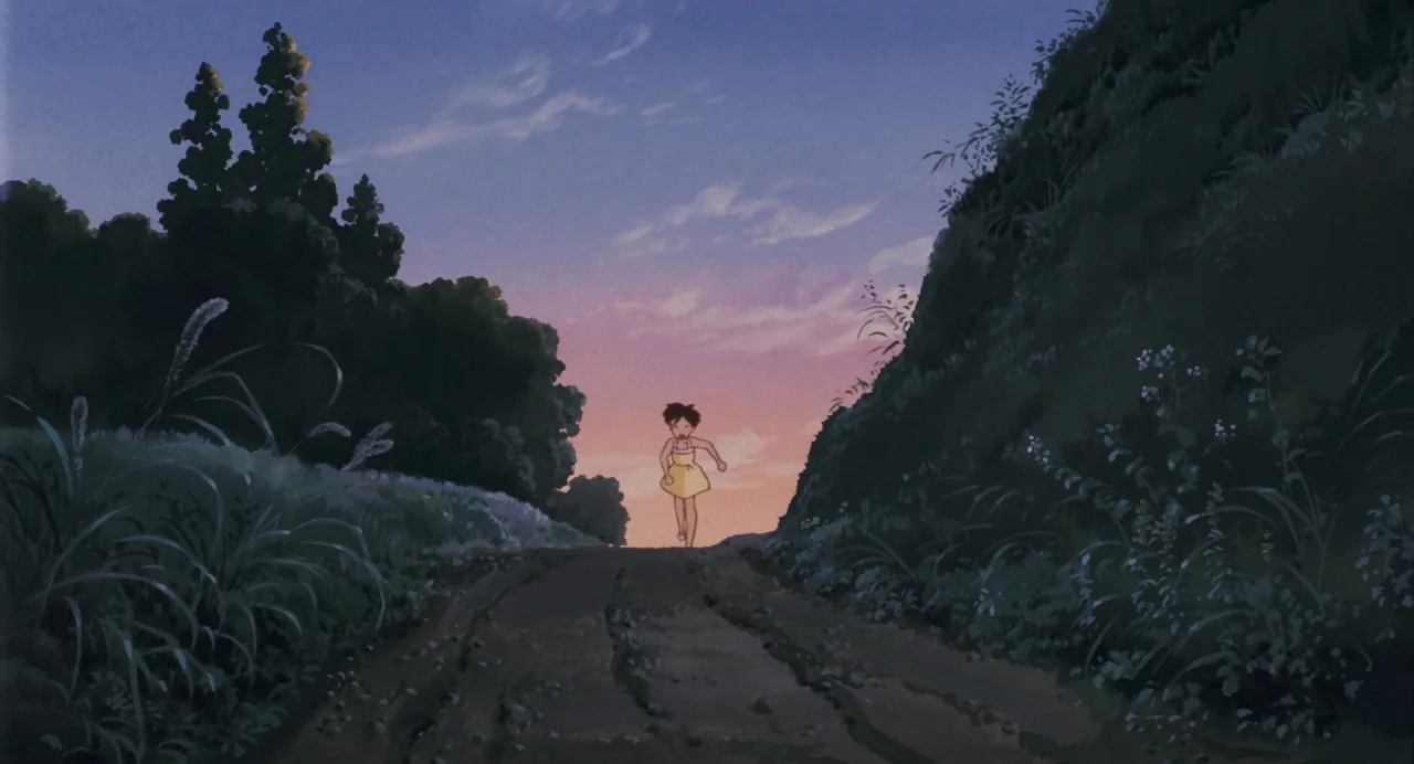 My Neighbour Totoro (1988) movie still: wide — A narrow dirt road passes through a dense, green countryside at dusk. A young girl in a yellow dress…