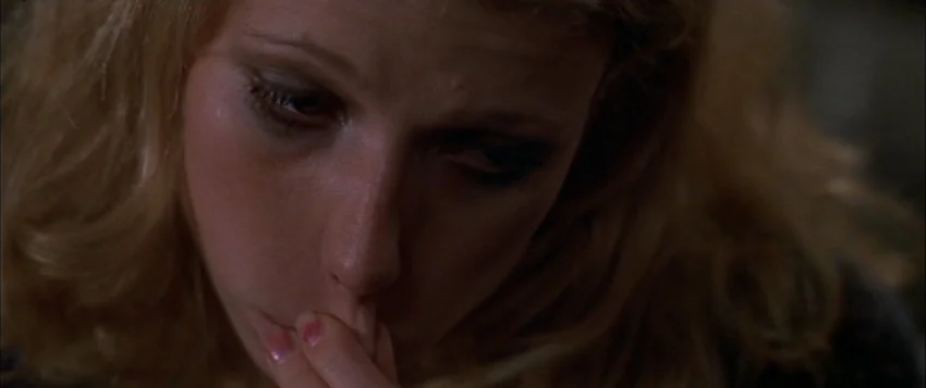 Hard Eight (1996) movie still: closeup — A close-up view of a young blonde woman in a dimly lit indoor space. She gazes downward while resting a…
