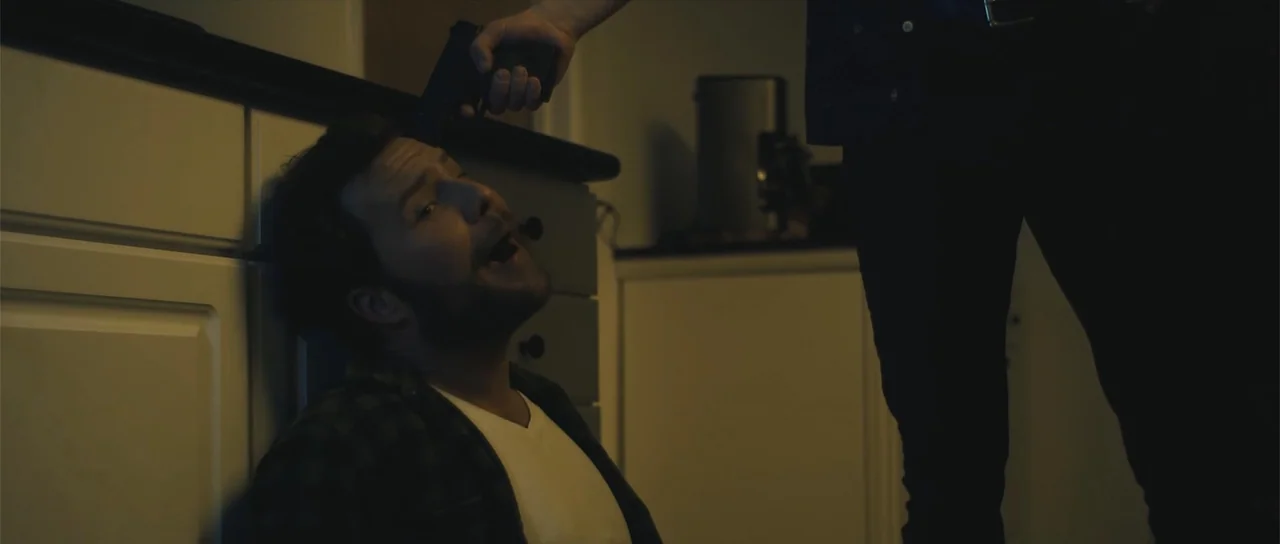 Night of the Missing (2023) movie still: medium — A dark kitchen interior features white cabinetry with black countertops. A man sits on the floor…