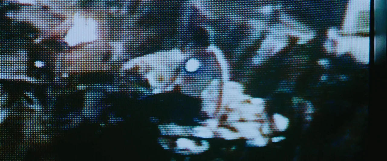 Iron Man (2008) movie still: closeup — A close-up view of a CRT television screen shows heavily pixelated, abstract imagery. The screen surface…