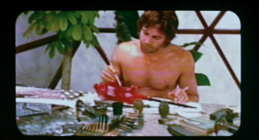 CQ (2001) movie still: medium — A man sits inside a white geodesic structure with large geometric window frames. He is bare-chested and concentrates…