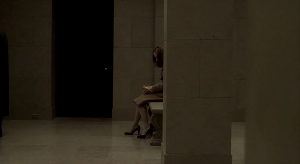 Birth (2004) movie still: wide — A spacious hall with large stone pillars and polished stone tile floors. A woman sits alone on a bench positioned…