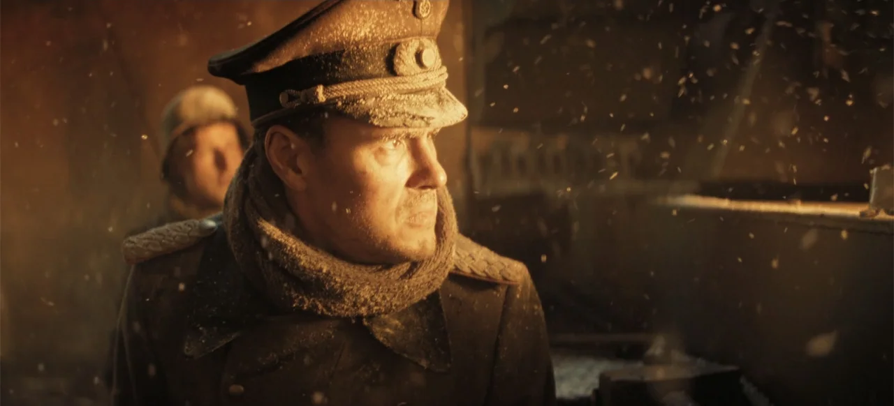 The Tank (2025) movie still: medium — Two men in German military uniforms stand inside an open military transport vehicle at night. Heavy snow falls…
