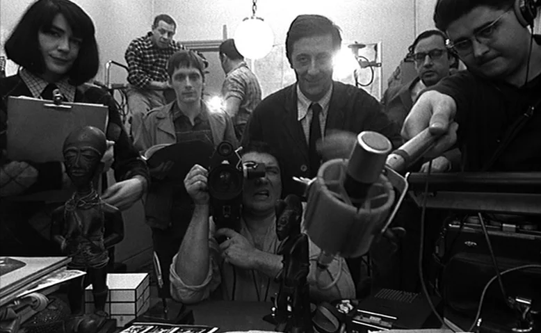 Who Are You, Polly Maggoo? (1966) movie still: medium — A crowded interior workspace holds multiple film crew members interacting with technical…