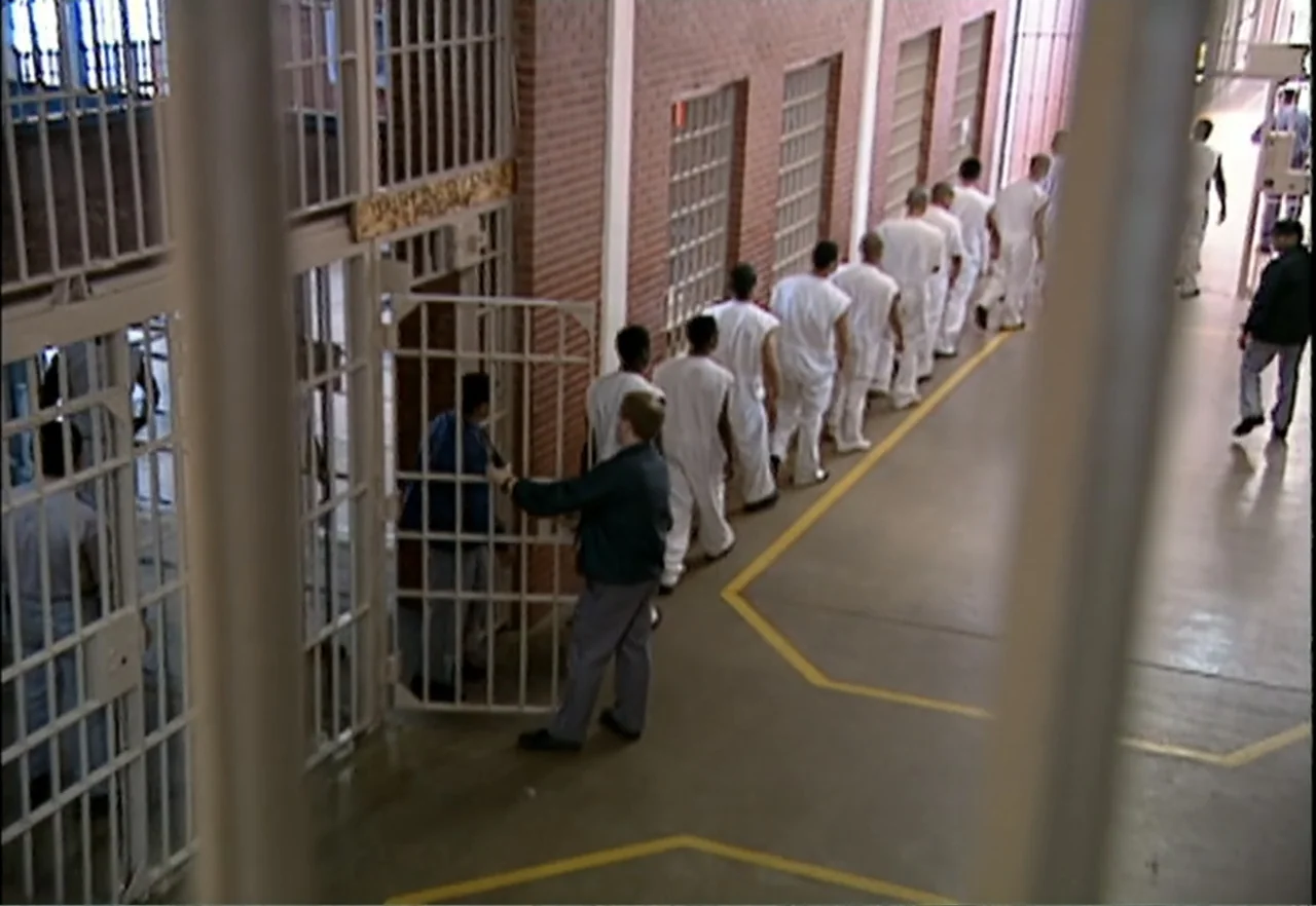 Broken Child (2000) movie still: wide — A long interior hallway features brick walls, multiple barred doors, and painted floor markings. A group of…