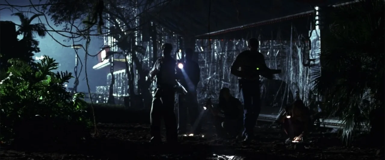 A Sound of Thunder (2005) movie still: wide — A dark outdoor area features dense foliage and silhouettes of several people searching ground. The…