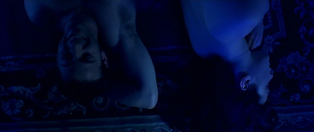 I Want You (1998) movie still: medium — A dark, carpeted space is illuminated by a deep blue light source. A man and a woman lie on the floor next…