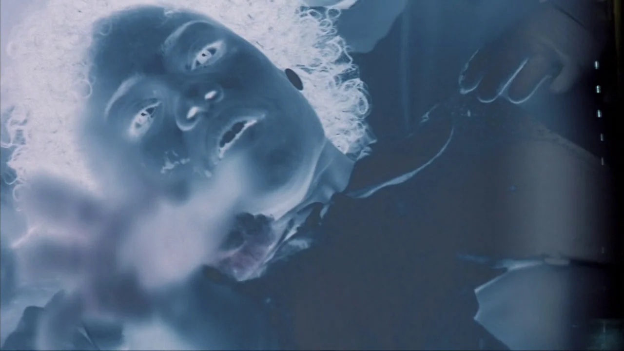 Blade II (2002) movie still: closeup — A person lies on their back in a dimly lit, undefined interior space. The subject reaches a hand toward the…