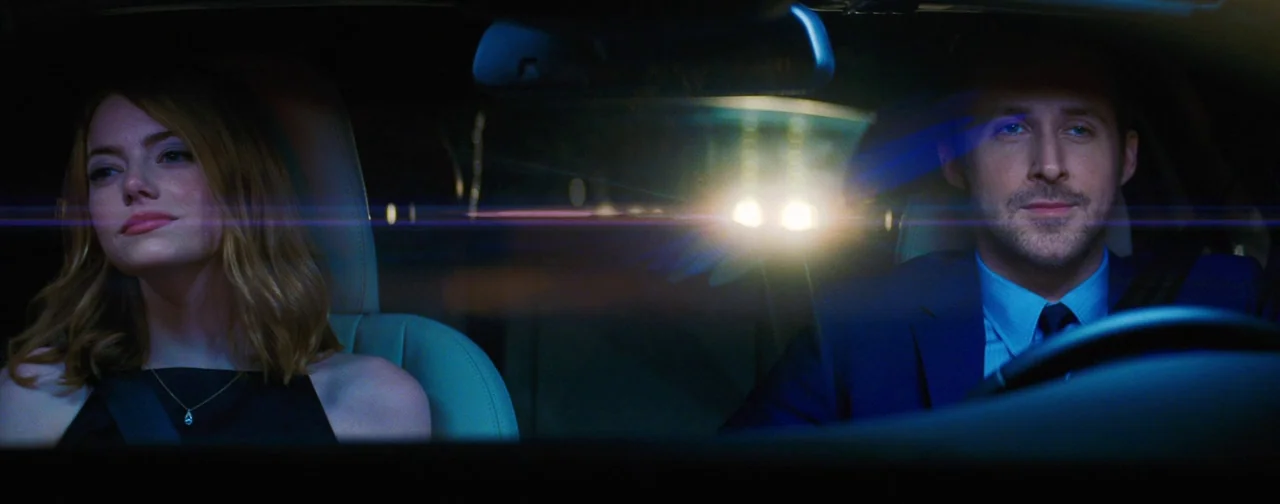 La La Land (2016) movie still: medium — A dark car interior at night with a man and woman in the front seats. An anamorphic lens flare stretches…