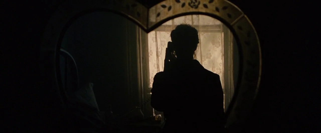Lost River (2014) movie still: medium — A dimly lit room with a window covered by ornate, floral-patterned curtains. A person stands before a…