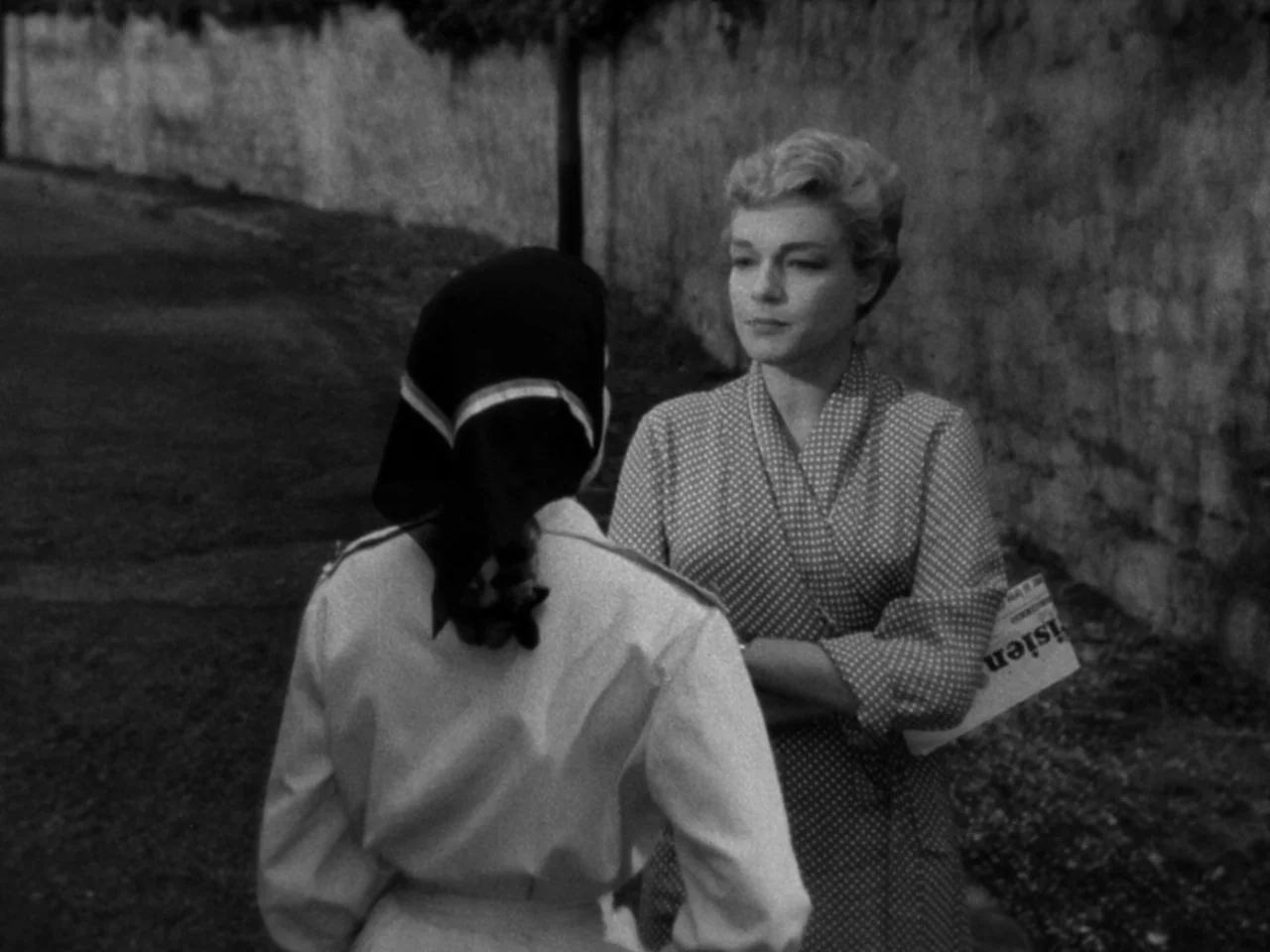 Diabolique (1955) movie still: medium — An outdoor path bordered by a high stone wall and a grass verge. Two women in mid-twentieth-century attire…