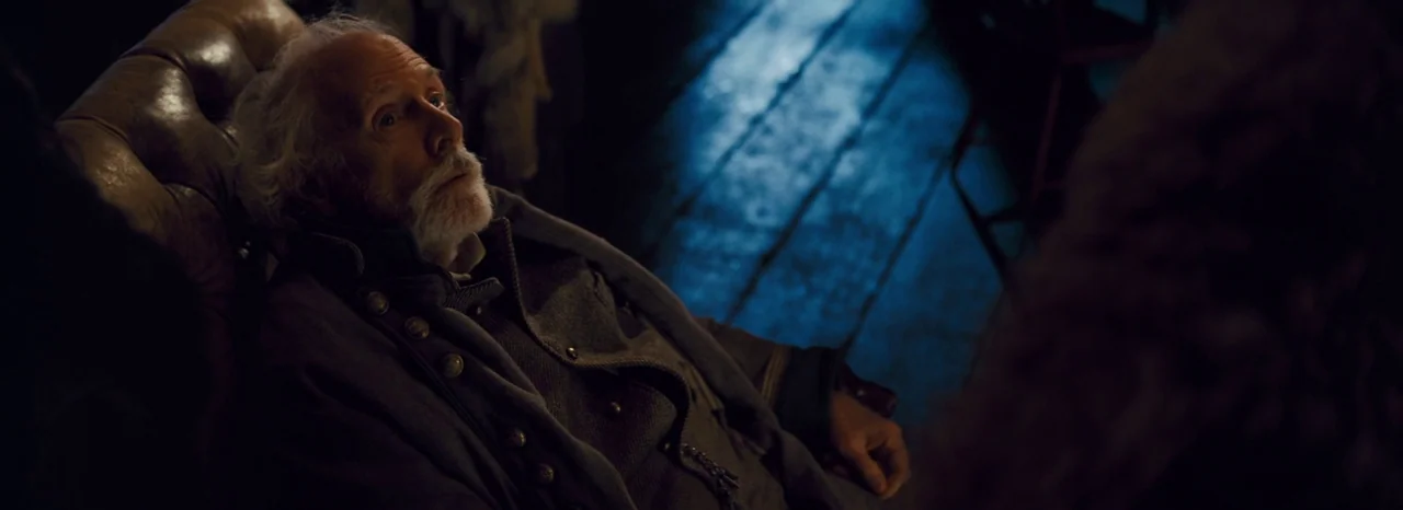 The Hateful Eight (2015) movie still: medium — An interior space with rough-hewn wooden floorboards and a dark leather armchair. An elderly man in a…