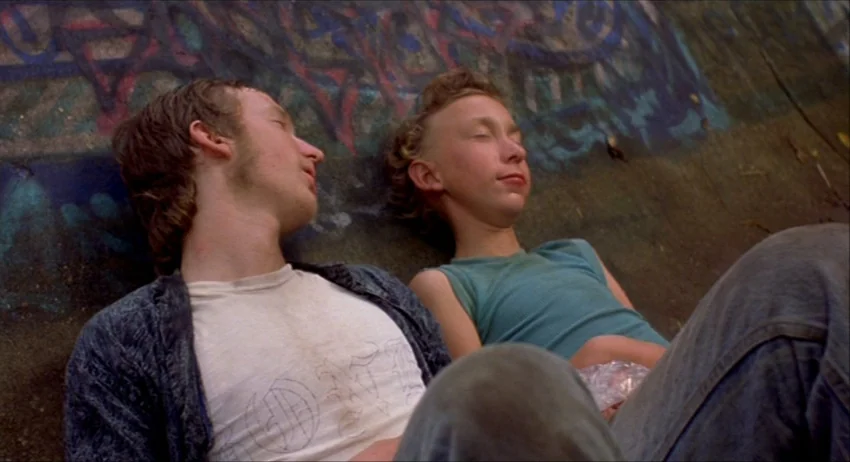 Gummo (1997) movie still: medium — Two young men lie against a concrete wall covered in blue and red graffiti. They both have their eyes closed…