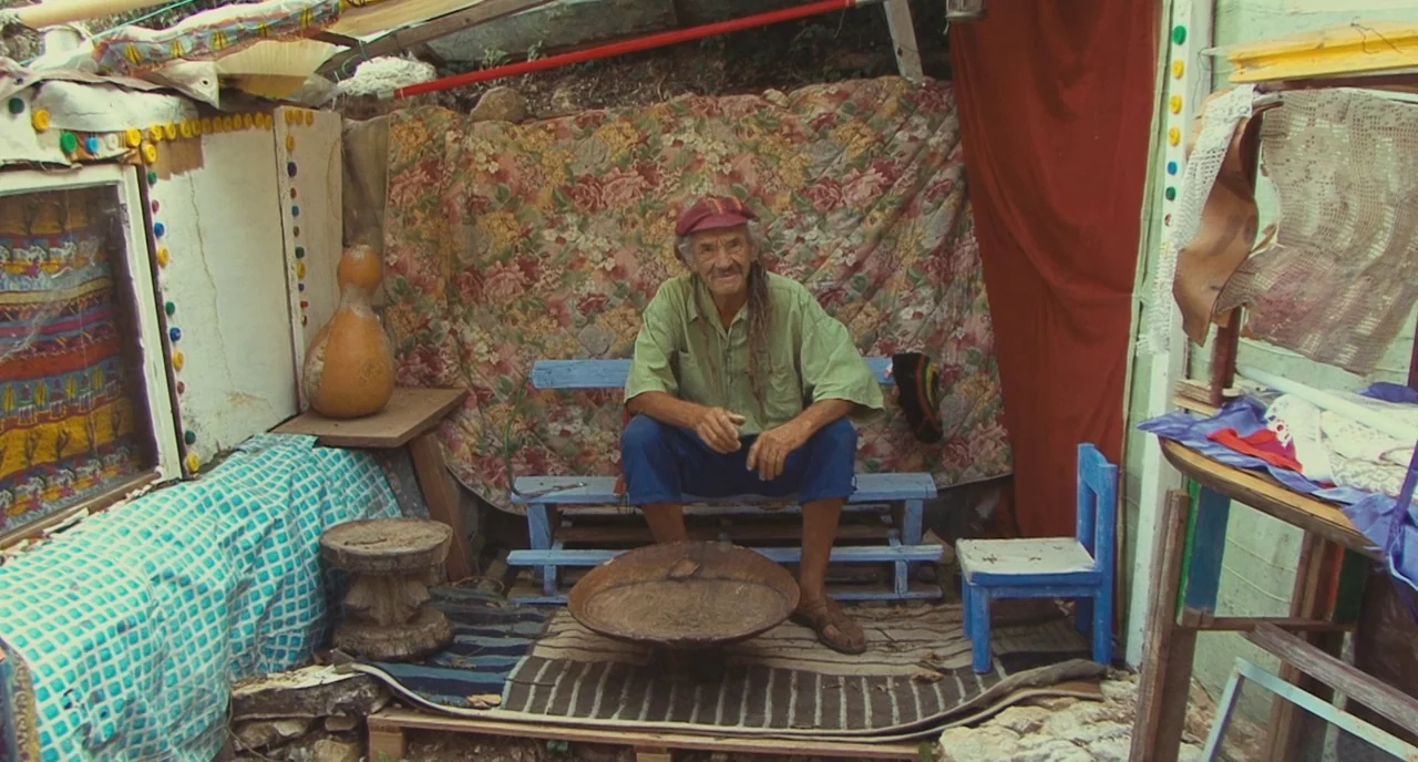 Faces Places (2017) movie still: fullbody — A makeshift shelter constructed from mismatched fabrics, wood panels, and colorful plastic bottle caps.…