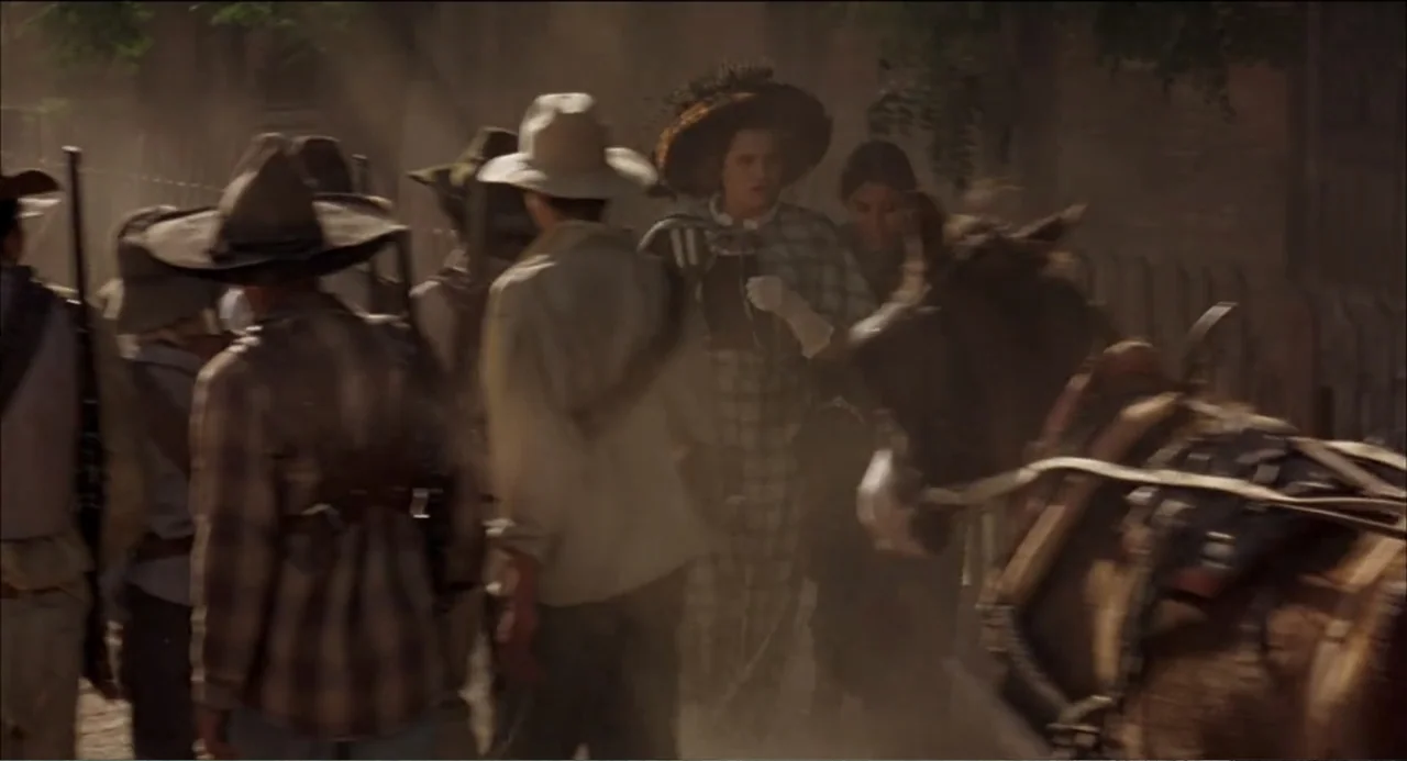 Like Water for Chocolate (1992) movie still: medium — A dusty 19th-century frontier street features wooden fences and low-visibility atmospheric…