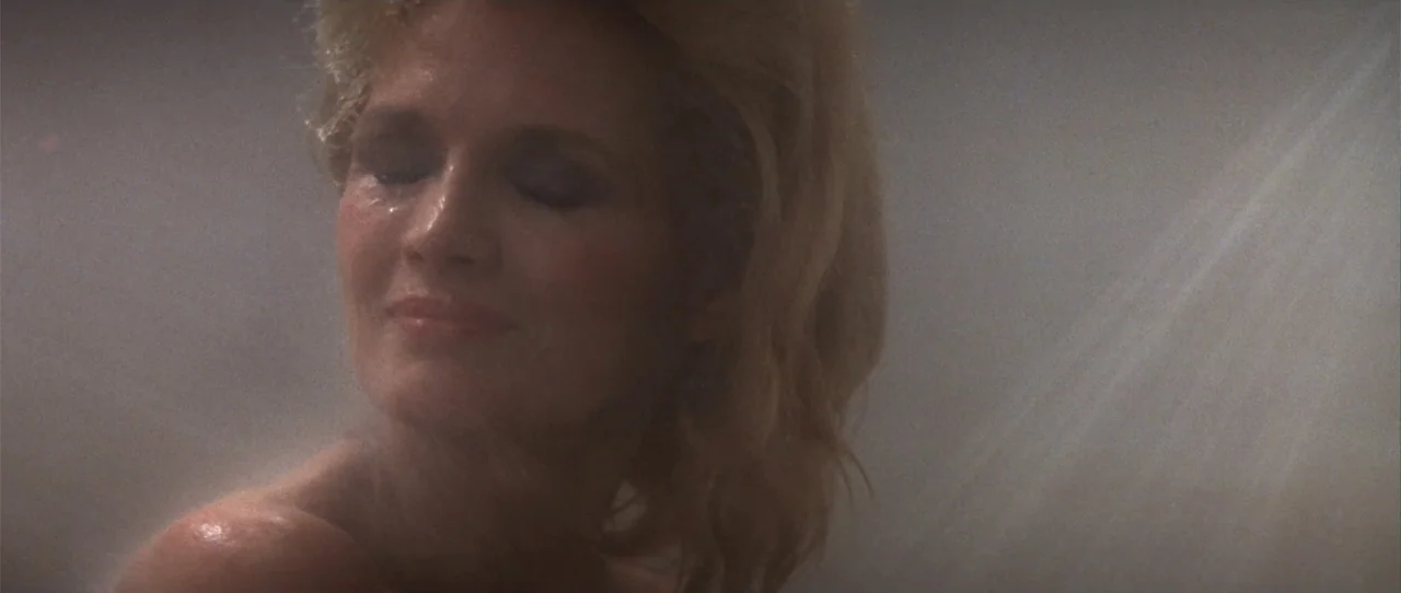 Dressed to Kill (1980) movie still: closeup — A tiled space filled with dense water mist and diffused light. A woman with wet blonde hair stands…
