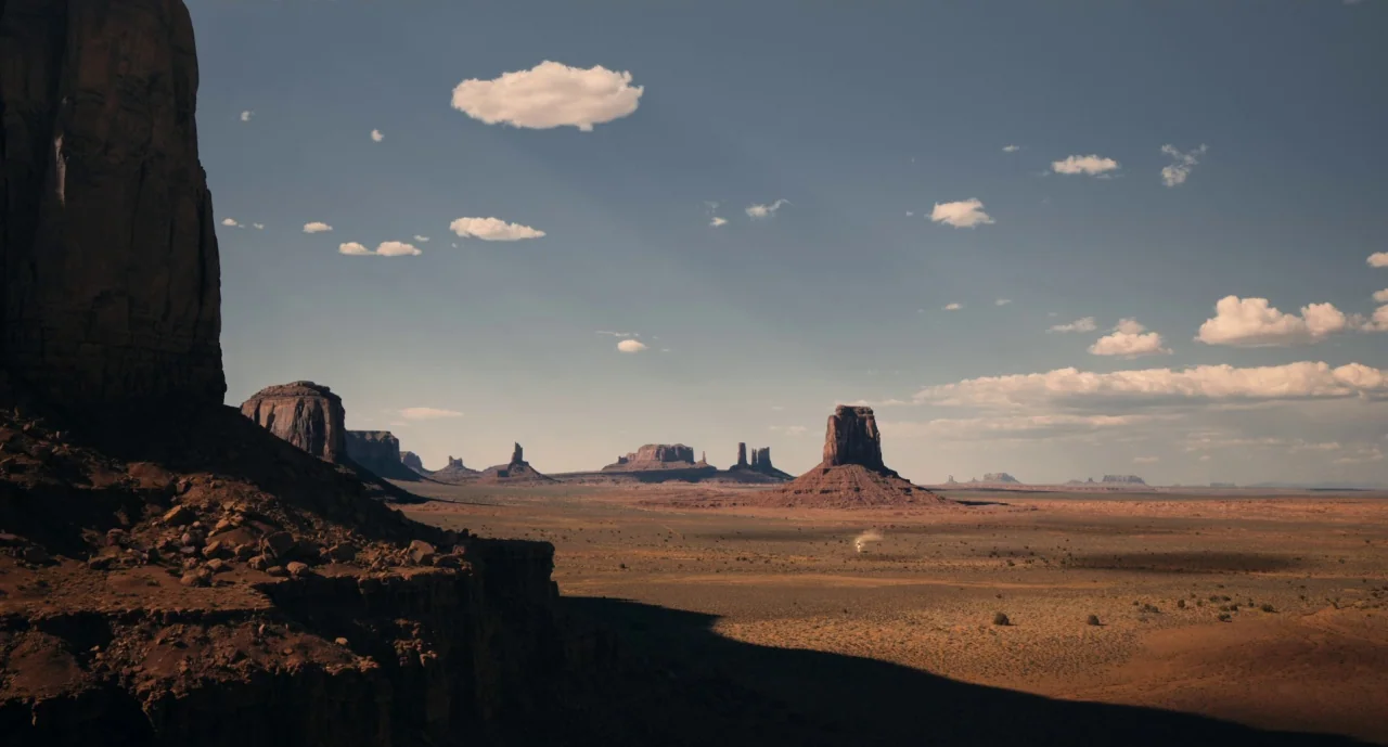 The Ballad of Buster Scruggs (2018) movie still: establishing — An expansive desert landscape features towering red sandstone mesas under a bright…
