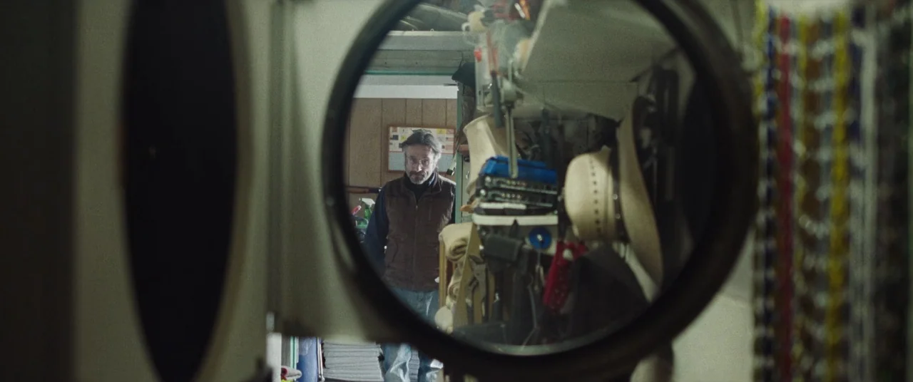 To Leslie (2022) movie still: medium — The view is framed through the circular door of a laundry machine. A man stands in the background of a…