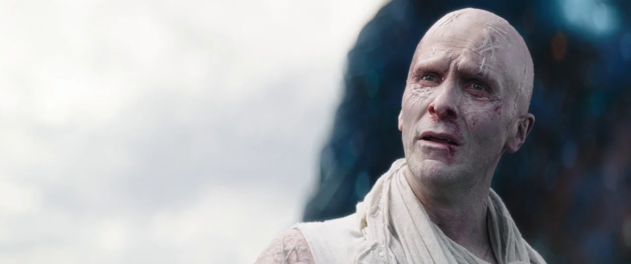 Thor: Love and Thunder (2022) movie still: closeup — A desolate landscape under a bright, cloudy sky serves as the backdrop. The subject, a pale man…