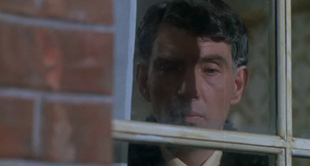 Blood From The Mummy’s Tomb (1971) movie still: closeup — A man's face is seen through the reflection and transparency of a window pane. The…