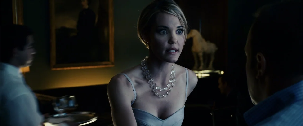 Zookeeper (2011) movie still: medium — A dimly lit room with dark walls, a framed painting, and a decorative horse sculpture. A blonde woman in a…