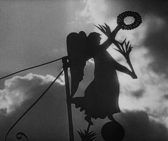 Vampyr (1932) movie still: closeup — A metal angel weather vane stands on a rooftop against a cloudy sky. The sculpture is rendered in silhouette…